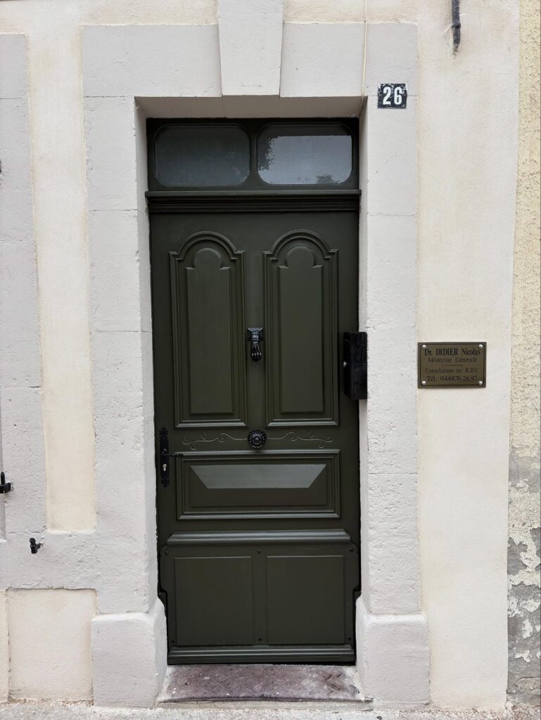 Entrée d'un cabinet médical : porte verte foncée avec heurtoir main, encadrement blanc, plaque "Dr. DIDIER Nicolas Médecine Générale 26".