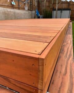 Gros plan sur la bordure d'une terrasse ou d'un spa en bois exotique rouge-brun, vissé, avec un arrière-plan flou de jardin et de clôture.