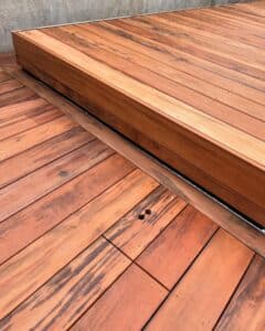 Terrasse en bois exotique brun-rouge avec des variations de grain foncé, montrant un rebord surélevé avec un joint noir.